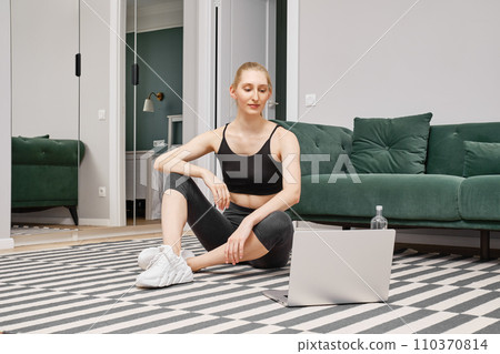 Young woman sits on the floor of her apartment and watching record with exercises Young woman sits on the floor of her apartment and watching record with exercises 110370814
