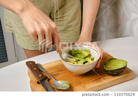 Woman mashes avocado pulp with a fork in a bowl Woman mashes avocado pulp with a fork in a bowl 110370829