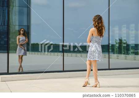 Woman looking at her reflection in glass wall of a building Woman looking at her reflection in glass wall of a building 110370865