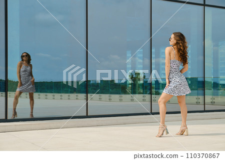 Woman enjoying her reflection in glass wall of a building Woman enjoying her reflection in glass wall of a building 110370867