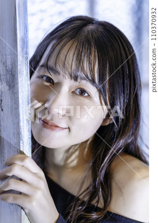 Young woman in a black dress peeping through the window 110370932