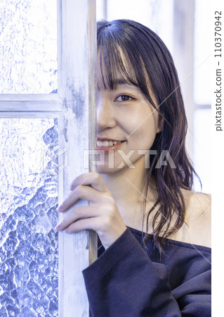 Young woman in a black dress peeping through the window 110370942