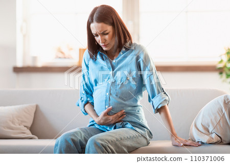 Expectant woman touches her belly in discomfort and pain indoors 110371006