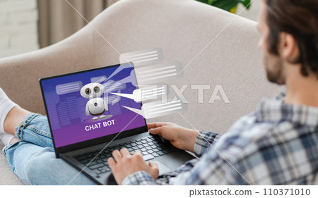 Unrecognizable man sitting on couch, using chatbot on laptop 110371010
