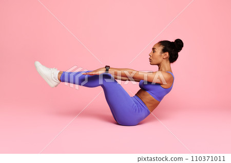 black woman practicing yoga making half boat pose, pink backdrop 110371011