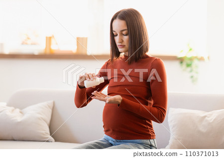 Expectant woman taking her daily vitamins sitting on couch indoors 110371013
