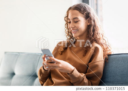 European adolescent girl browsing internet on phone in cozy home European adolescent girl browsing internet on phone in cozy home 110371015