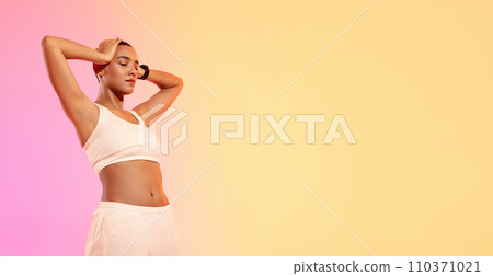 A serene woman with a shaved head stands with eyes closed and hands behind head A serene woman with a shaved head stands with eyes closed and hands behind head 110371021