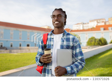 African college student guy stands holding laptop and coffee outside African college student guy stands holding laptop and coffee outside 110371026