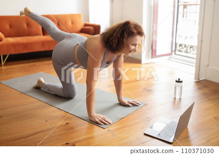 Senior woman exercises with online class at home, using laptop 110371030