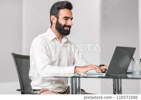 Smiling hindu man working on laptop in a bright office 110371086