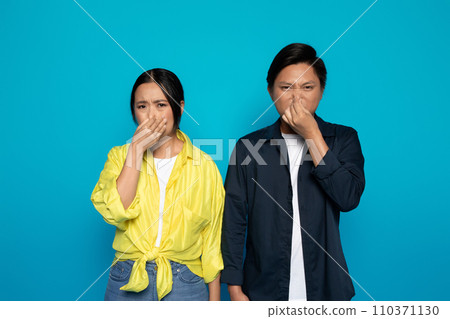 Two Asian individuals are holding their noses with disgusted expressions 110371130