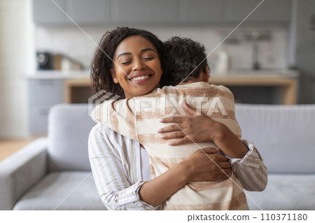 Smiling black mother warmly embracing her preteen son at home Smiling black mother warmly embracing her preteen son at home 110371180
