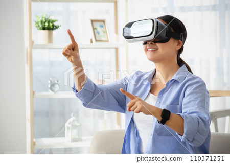 Emotional young asian woman in VR glasses sitting on couch Emotional young asian woman in VR glasses sitting on couch 110371251