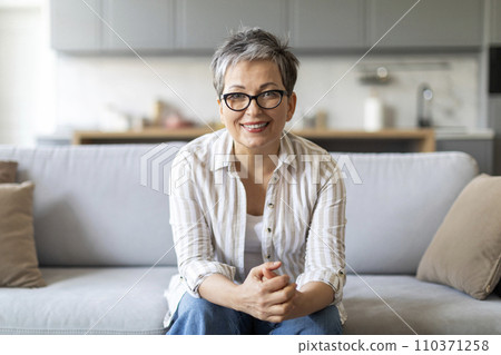 Smiling elderly woman sitting on couch in living room interior 110371258
