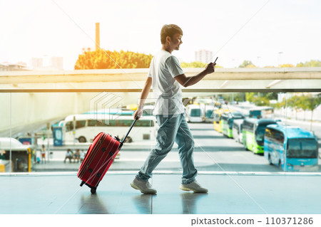 Side view asian guy tourist walking by airport with smartphone Side view asian guy tourist walking by airport with smartphone 110371286