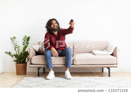 Indian man holding remote control relaxing with TV at home Indian man holding remote control relaxing with TV at home 110371326