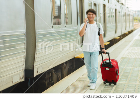 Chinese guy tourist walking by train station, talking on phone Chinese guy tourist walking by train station, talking on phone 110371409
