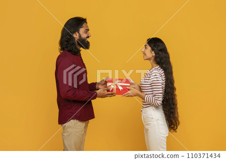 Cute young eastern couple exchanging gifts on yellow background Cute young eastern couple exchanging gifts on yellow background 110371434
