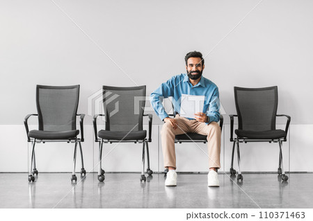 Smiling indian man sitting with document in a row of chairs 110371463