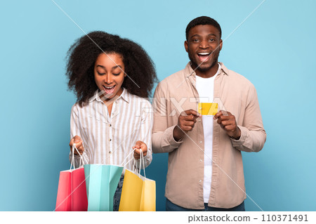 Excited black couple with colorful shopping bags and credit card on blue background 110371491