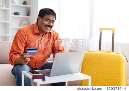 Happy mature indian man using laptop, buying tour on internet 110371644