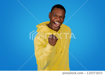 An exuberant African man in a yellow hoodie punches the air with a clenched fist 110371653