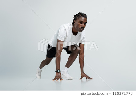 Focused black man in athletic wear poised in starting position for sprint Focused black man in athletic wear poised in starting position for sprint 110371773