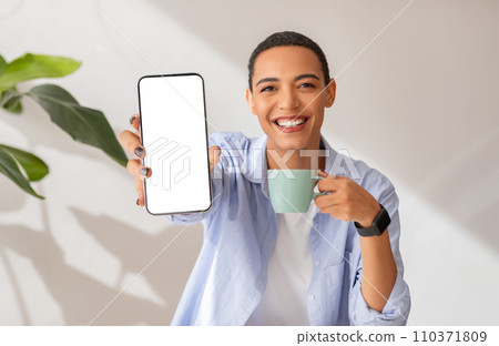 Smiling woman showing a blank smartphone screen while holding a coffee mug Smiling woman showing a blank smartphone screen while holding a coffee mug 110371809