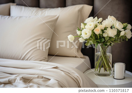 Beautiful white roses in a vase on a table next to bed with gorgeous organic linens Beautiful white roses in a vase on a table next to bed with gorgeous organic linens 110371817