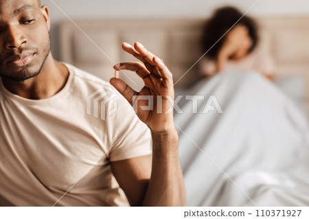 black man taking potency pill sitting in bed with girlfriend 110371927