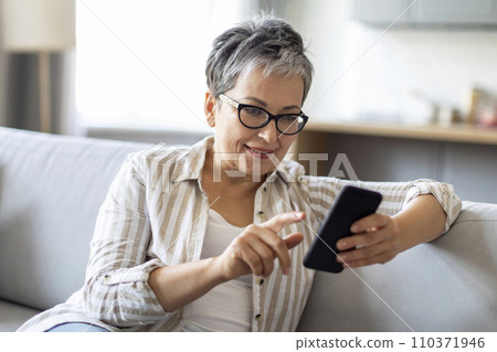 Great App. Senior Woman Using Smartphone While Sitting On Couch At Home Great App. Senior Woman Using Smartphone While Sitting On Couch At Home 110371946