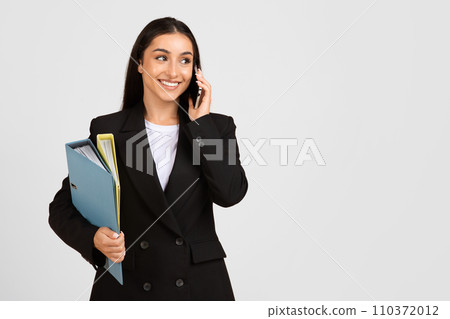 Businesswoman on phone with documents in hand, smiling Businesswoman on phone with documents in hand, smiling 110372012