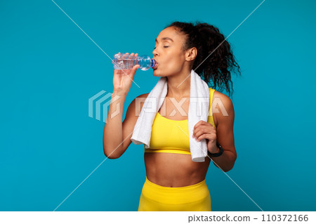 Fit black woman in sportswear sipping water from bottle, studio 110372166