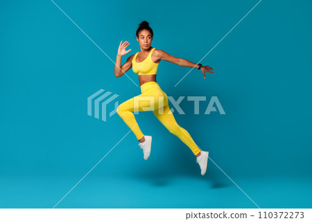 Determined African American fitness woman jumps against blue studio background 110372273