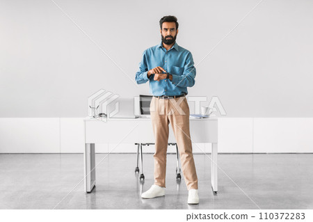 Indian businessman checking time, standing by office desk 110372283