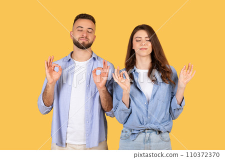 Cheerful european couple show ok gesture with hands, meditating with closed eyes, enjoy lifestyle, breathing exercises 110372370