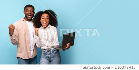Joyful black pair with laptop shaking fists, panorama, free space 110372413