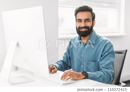 Confident indian businessman working at computer in office interior 110372425