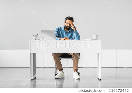 Stressed indian businessman with hand on forehead at desk 110372432