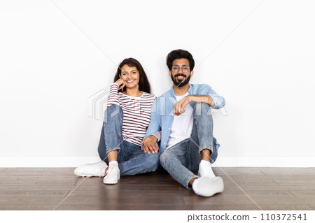Hindu couple sitting on floor over white blank wall background 110372541