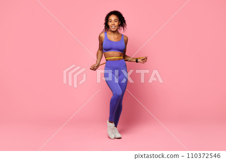 Young athletic black woman measuring waist showcasing fitness progress, studio 110372546