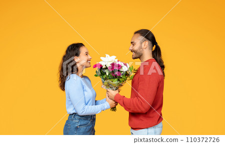 Man giving his happy girlfriend flowers, orange background Man giving his happy girlfriend flowers, orange background 110372726