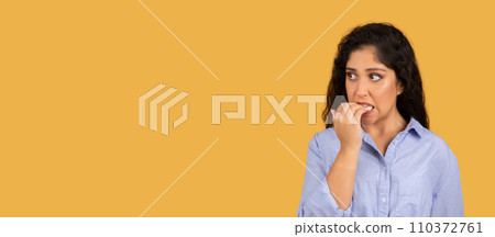 Anxious young woman with curly hair biting her nails and looking away with a worried expression 110372761
