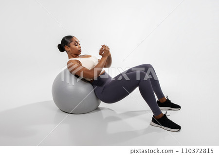 african woman doing abs exercises on fitness ball, white backdrop african woman doing abs exercises on fitness ball, white backdrop 110372815