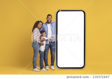 Happy Black Family Of Three Posing Near Blank Smartphone With White Screen Happy Black Family Of Three Posing Near Blank Smartphone With White Screen 110372847