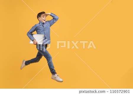 Teen boy holding laptop while running on yellow background Teen boy holding laptop while running on yellow background 110372901