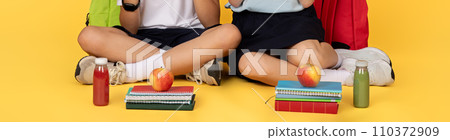 Schoolchildren sitting cross-legged with healthy snacks and notebooks 110372909