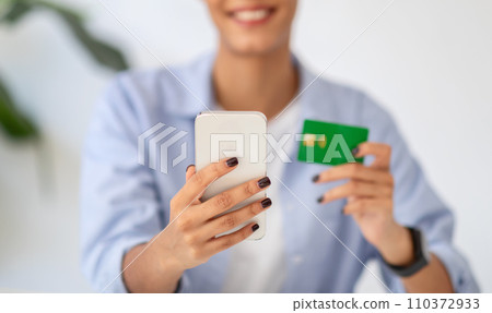 Blurred young woman smiling while holding a smartphone and credit card 110372933
