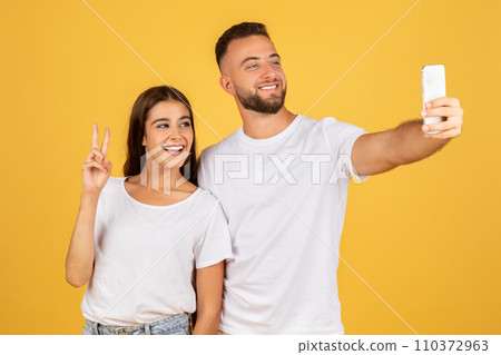 A beaming young woman flashes a peace sign while taking a selfie with a smiling man 110372963